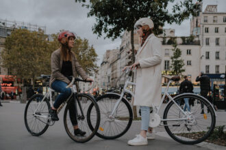 Deux cyclistes portant des casques vélo vintage discutent à l'arrêt dans une rue parisienne