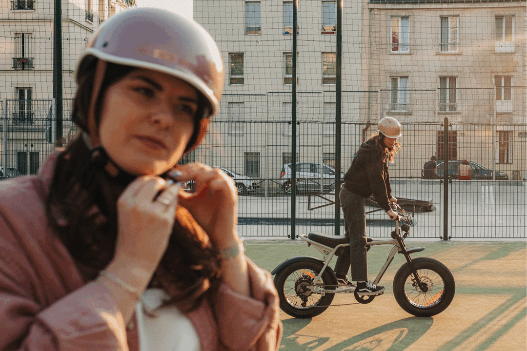 Cycliste ajustant son casque vélo vintage blanc devant un immeuble parisien, un autre cycliste en arrière-plan