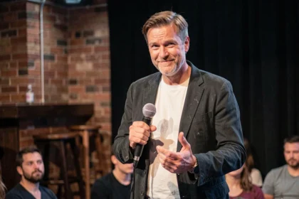 Comédien de stand-up tenant un micro avec une expression malicieuse sur scène dans un club de comédie intime